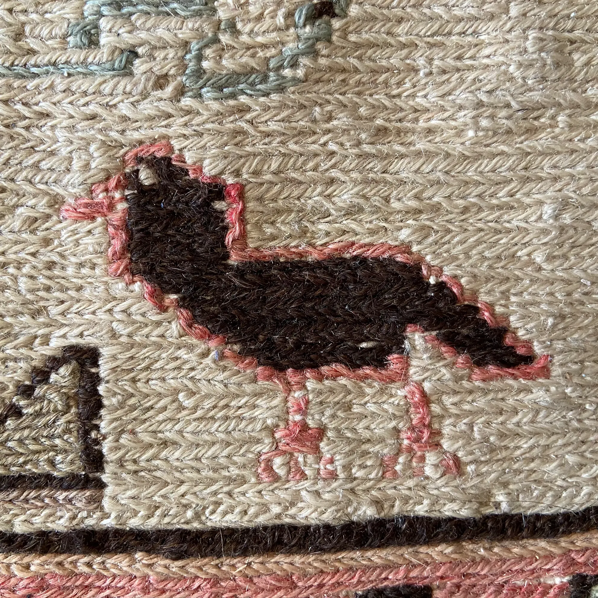 selver yıldırım: close-up of a traditional textile with an embroidered bird in black and pink on a beige woven background.