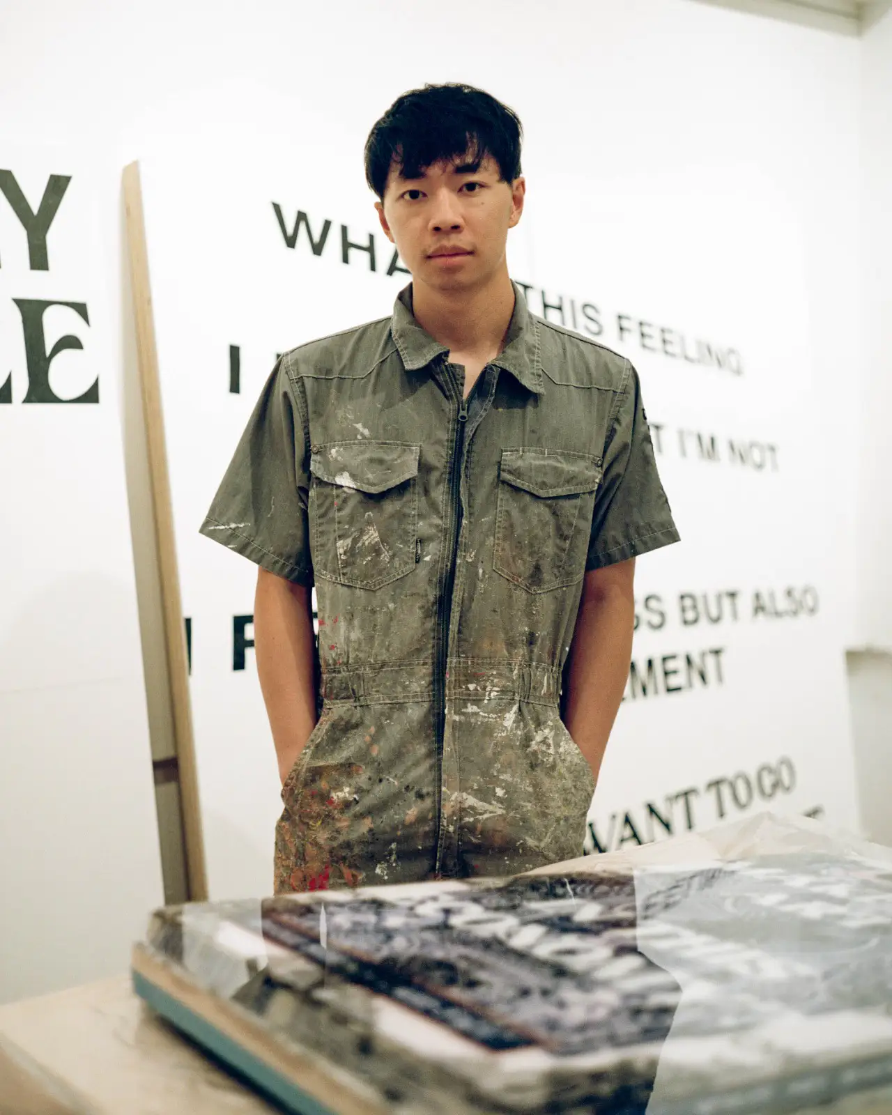 michael rikio ming hee ho standing in his studio with text-based artworks promising artist of tomorrow now 