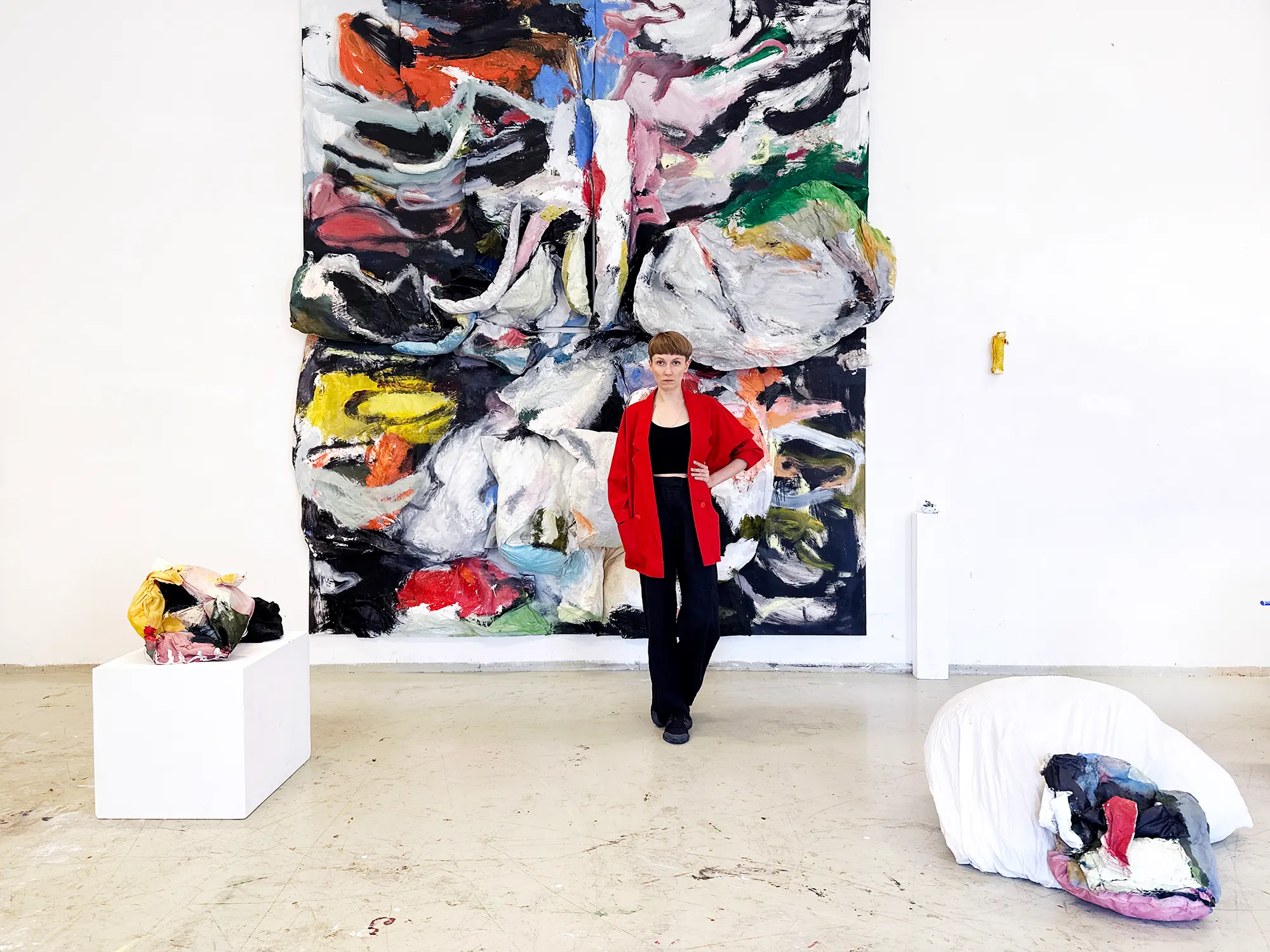 olga shcheblykina standing in front of her abstract, colorful artwork with sculptures on the floo